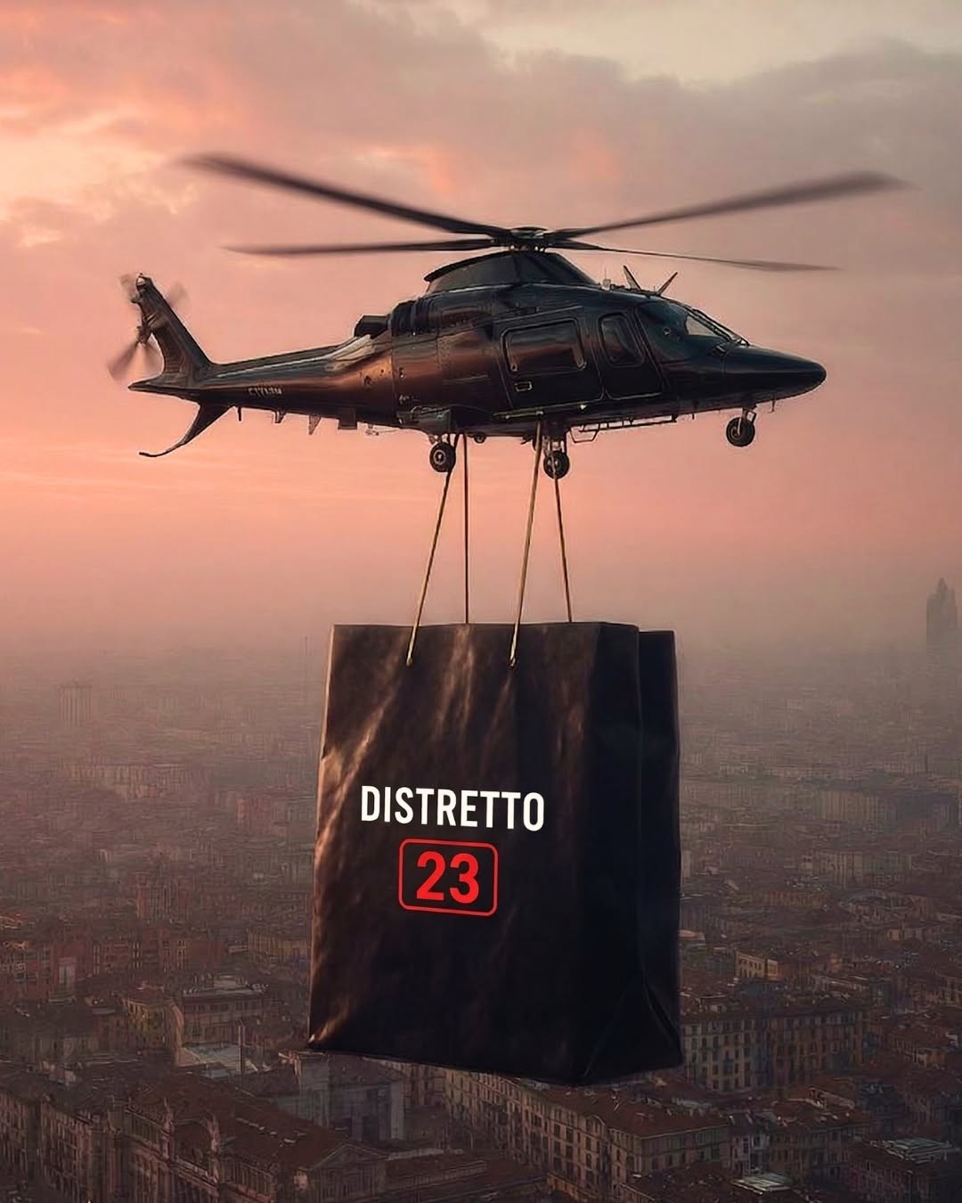 Elicottero nero che trasporta una grande shopper scura con scritta DISTRETTO 23 sopra una città al tramonto rosa